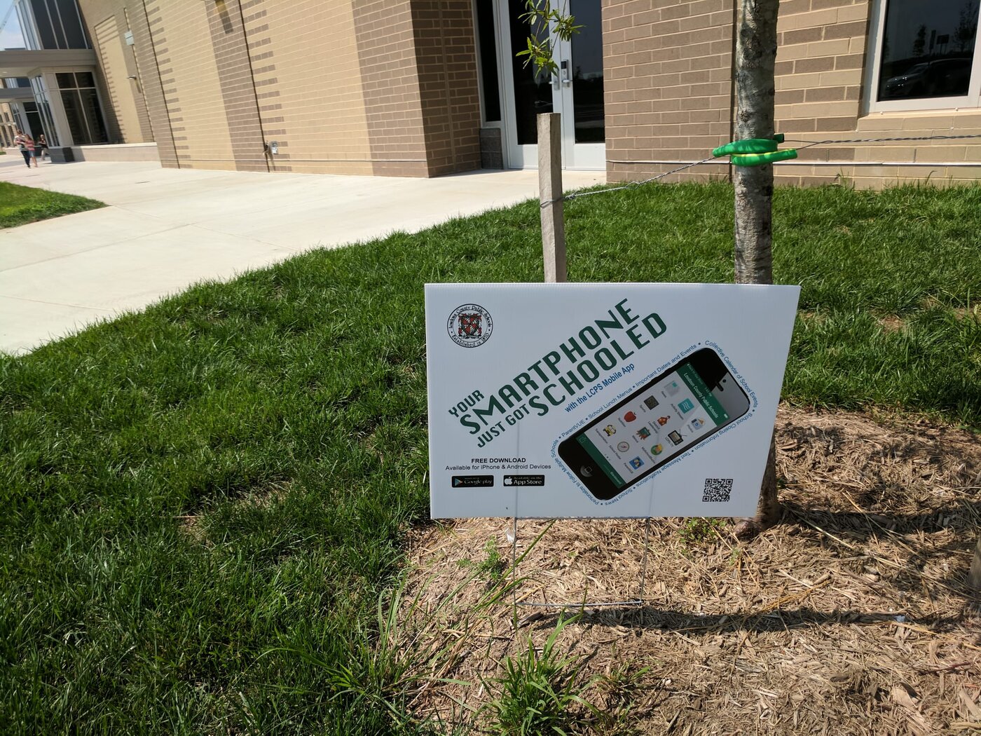 Outdoor lawn sign advertising a school app with a phone graphic, QR code, and 'free download' label
